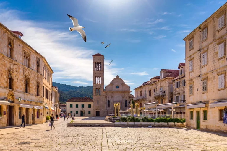 Hauptplatz in der alten mittelalterlichen Stadt Hvar mit überfliegenden Möwen. Hvar ist im Sommer eines der beliebtesten Reiseziele in Kroatien. Zentraler Pjaca-Platz in der Stadt Hvar, Dalmatien, Kroatien.