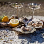 Romantische Genießerorgie an der Meeresküste Frisch gepflückte Austern mit Bio-Zitrone und mediterranen Kräutern mit silbernen Champagnergläsern