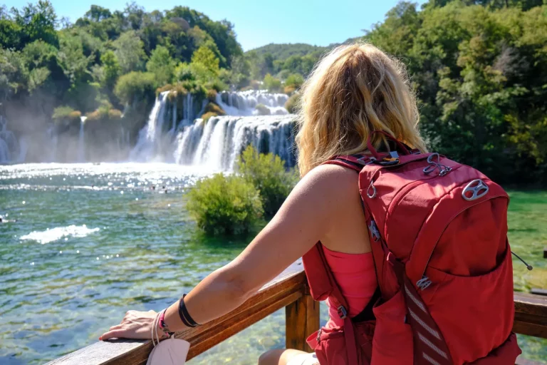 Touristin mit Rucksack bewundert den Wasserfall Skradinski Buk im Krka-Nationalpark. Tourismus, Kroatien, Sommer.